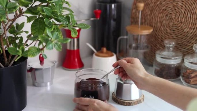 女性双手将研磨咖啡倒入现代厨房背景下的土耳其铜咖啡冲泡壶中。早餐咖啡概念。在家煮咖啡的过程。慢动作