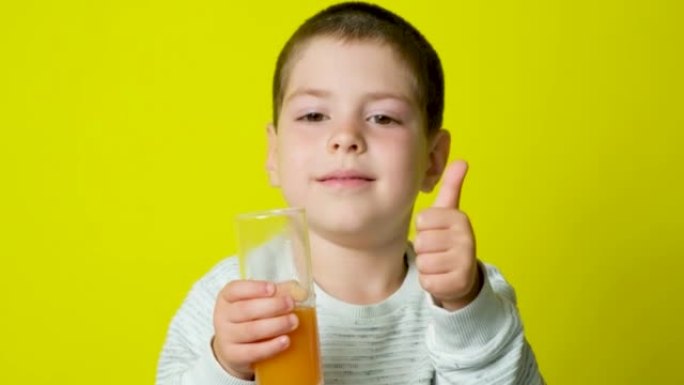 一个快乐的孩子喝橙汁，在黄色背景上竖起大拇指。