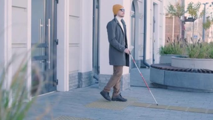 盲人在直的触觉瓷砖上使用白色手杖来导航道路