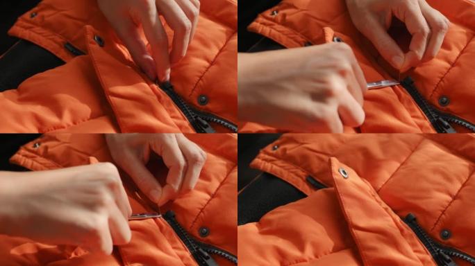 女性的手在冬季夹克，羽绒服的橙色防水织物上用剪刀剪线。纺织、服装生产，秋季亮丽夹克。时尚，时尚。衣服