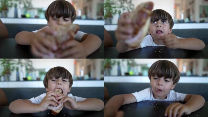 一个小男孩抓着面包，坐在桌子上吃了一口碳水化合物食物