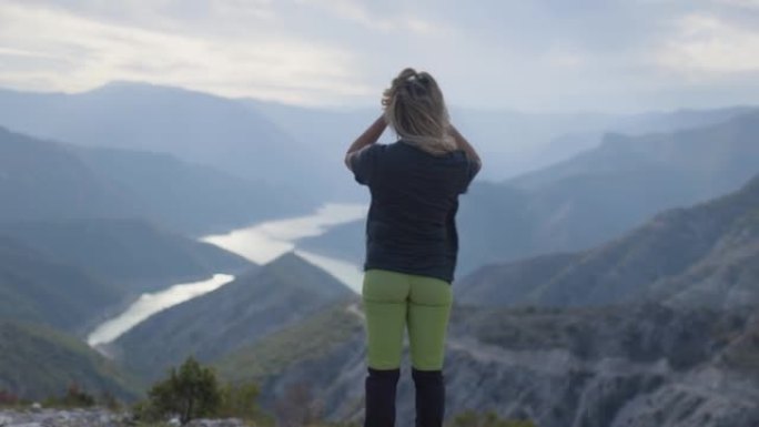 远足女孩从山上高处欣赏河湖美景。站在多云多风的天气里。