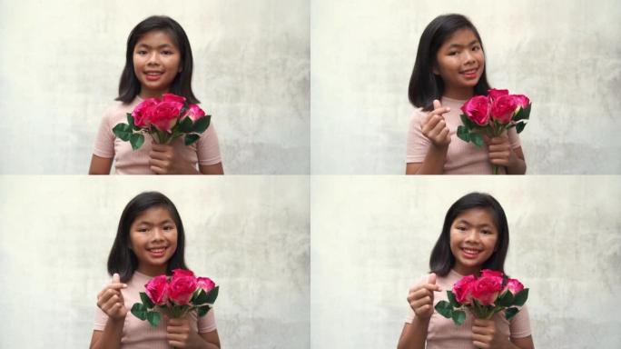 亚洲少女手持一束粉红玫瑰，摆迷你心示意我爱你的标志，白色旧墙背景