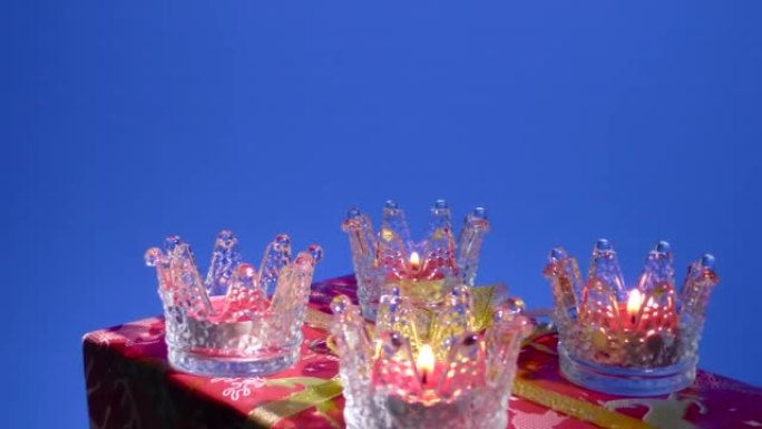 在蓝色背景上，玻璃架中的新年蜡烛在一个大礼物上旋转