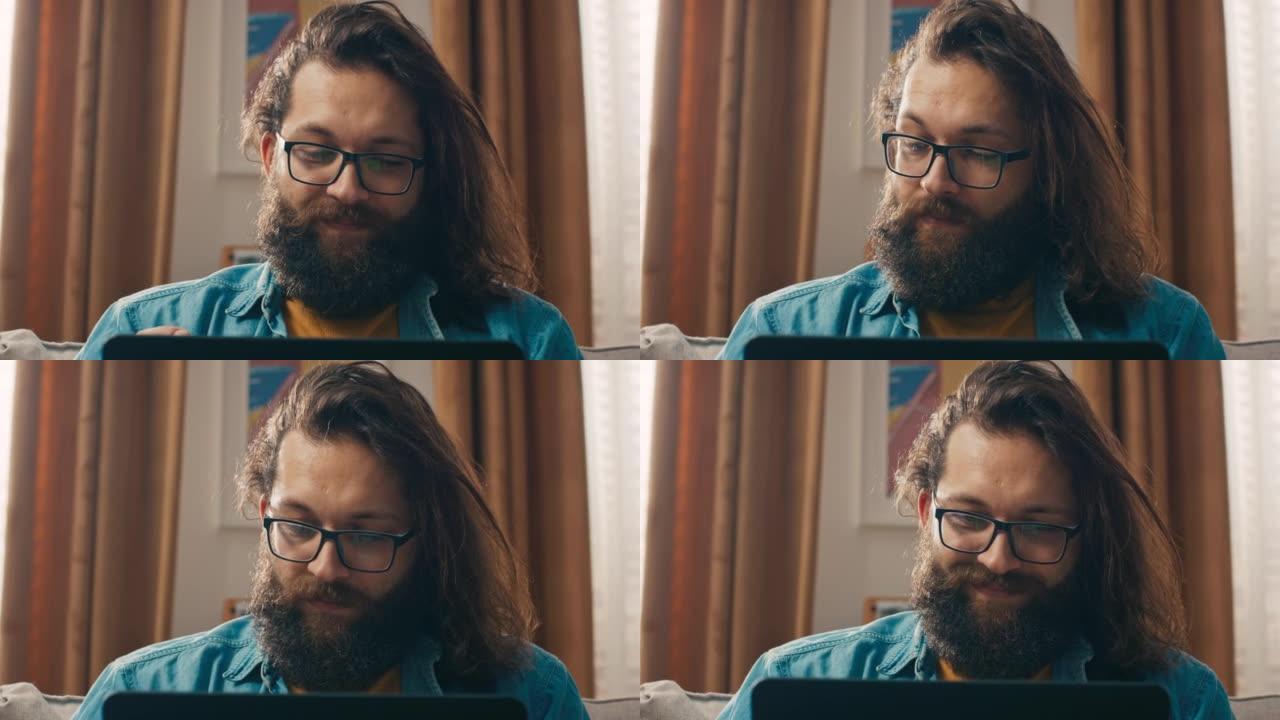 戴着眼镜的大胡子时髦男人的脸的特写镜头在笔记本电脑上浏览互联网，网上商店为亲人寻找礼物，家居饰品