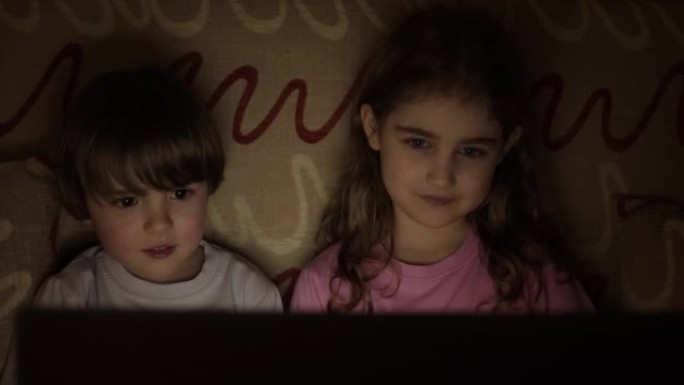 在笔记本电脑上看电视时，给小孩子画像。男孩和女孩在客厅的笔记本电脑上观看卡通。概念电子游戏，娱乐，情