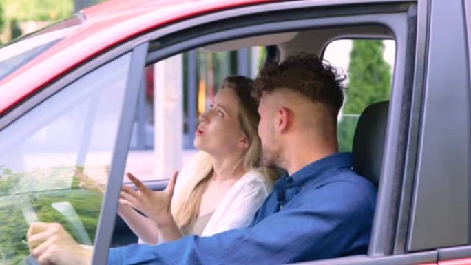 白人积极的女人坐在汽车的前排座位上，与男友在情感上交谈，讲述了一些事情。年轻夫妇坐在红色汽车上。运输