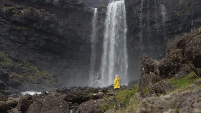 丹麦法罗群岛瀑布前穿着黄色雨衣的金发女子
