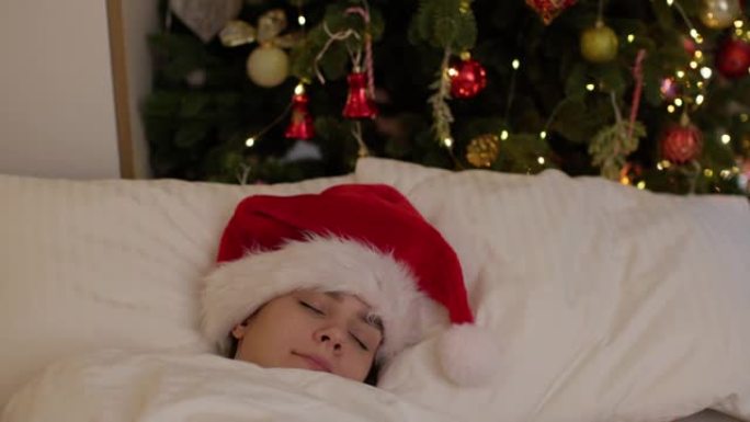 漂亮的年轻女子圣诞老人帽子睡床附近装饰的圣诞树