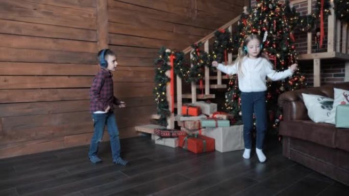 全长拍摄的孩子戴着耳机听音乐，在圣诞树附近跳舞玩得开心。有小孩的幸福家庭庆祝平安夜节日，在圣诞节的房