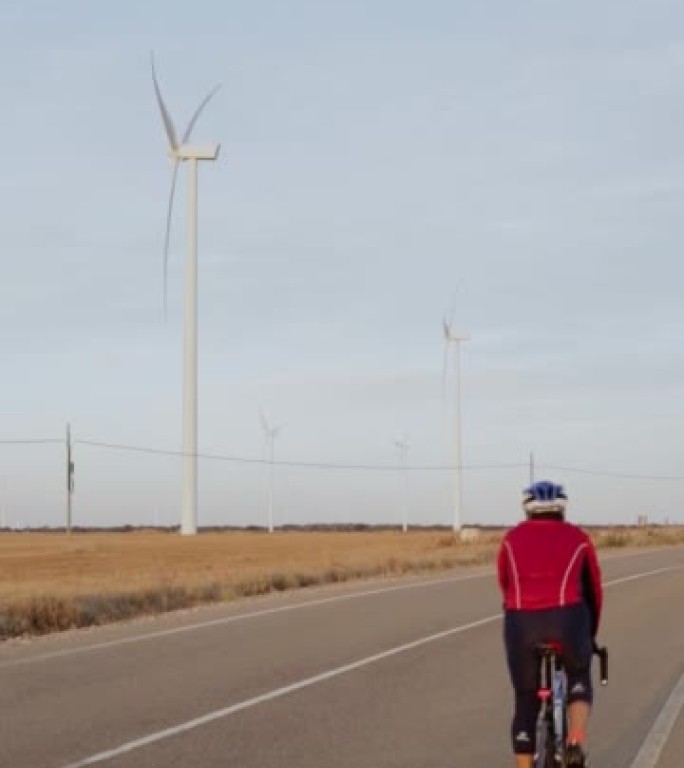骑自行车的人从风电场旁边行驶的垂直视频