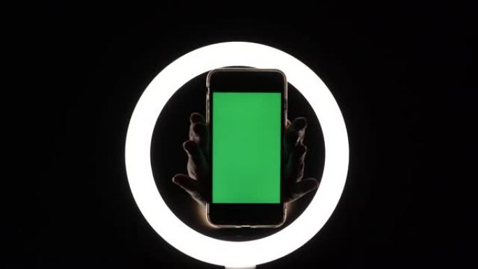女性双手在黑色背景上显示手机特写。插入广告的绿屏模型