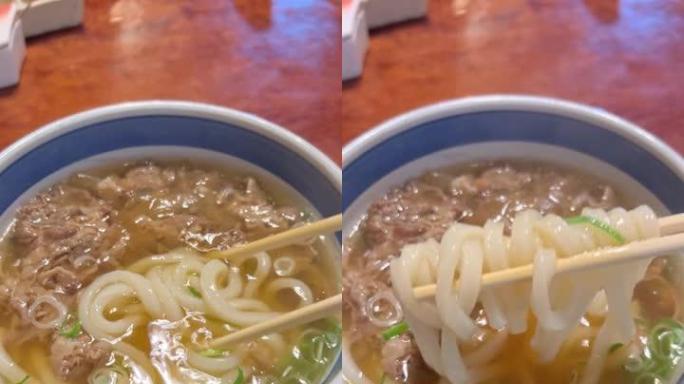 垂直烹饪视频，日本牛肉乌冬面的运动与清汤。用筷子吃一口饭。一碗热的新鲜煮熟的牛肉乌冬面汤。大石肉汤供