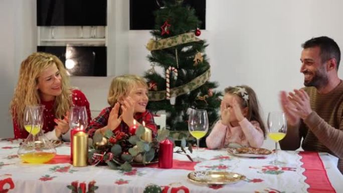 一家人在家里吃晚饭，用传统的食物和装饰庆祝平安夜，他们坐在圣诞树旁边的桌子旁，高兴地鼓掌。