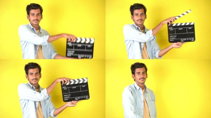 开朗的年轻亚洲印度男子站在隔板上，拍板用于电影制作，孤立在彩色背景工作室肖像上