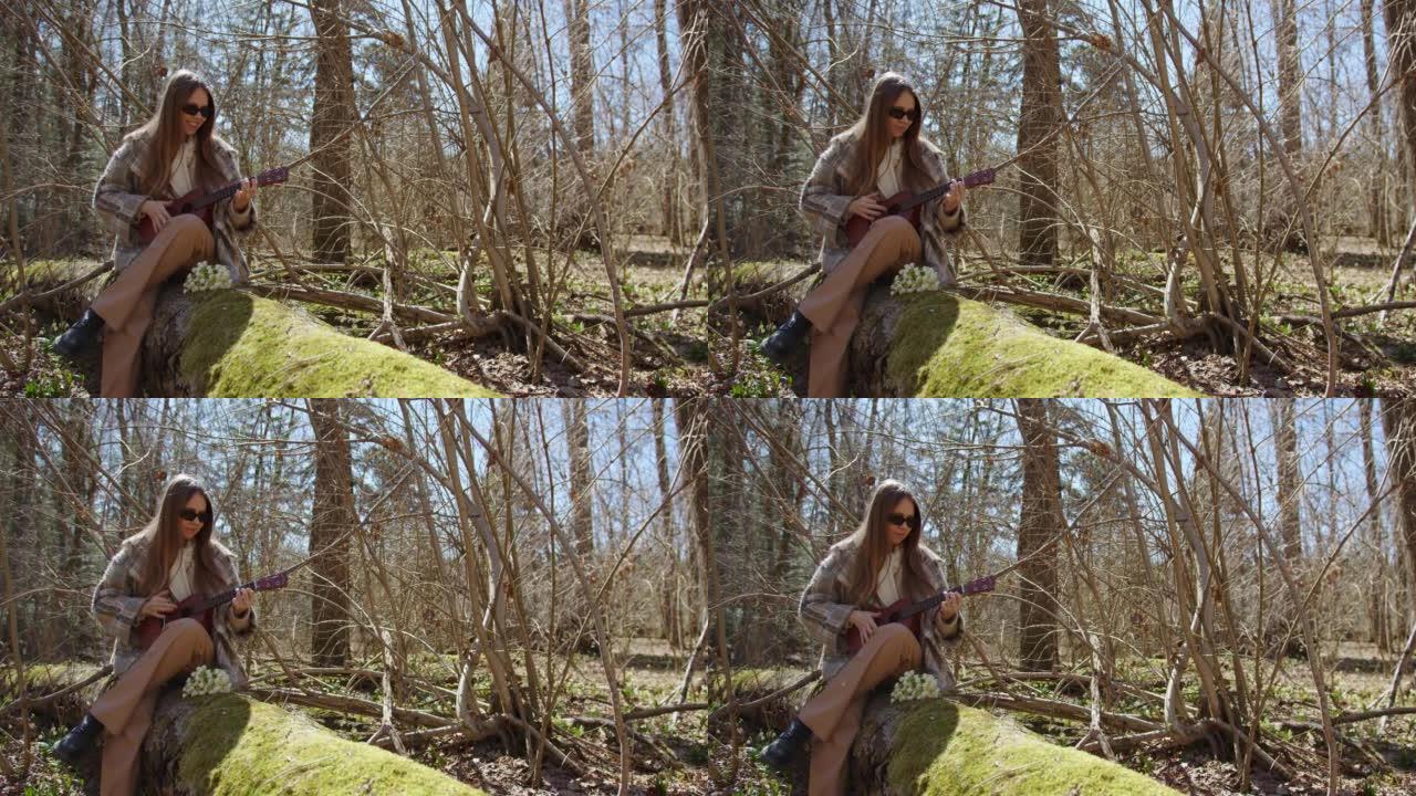 戴墨镜的女孩坐在鲜花丛中的森林中倒下的原木上，玩夏威夷四弦琴