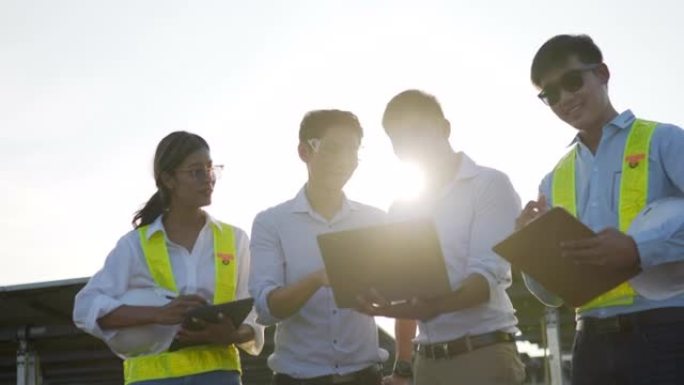 背光镜头，一组亚洲工程团队在计划操作和站内光伏太阳能电池板使用笔记本电脑和平板电脑，年轻的检查员工程