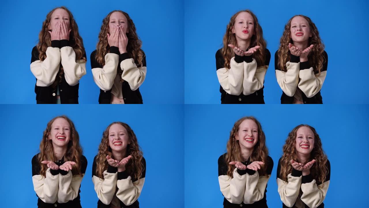 双胞胎女孩在蓝色背景上发送空中吻的4k视频。