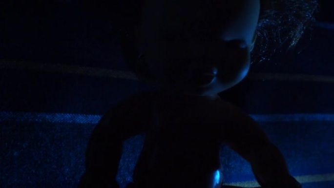 黑暗中有红色和蓝色灯光的可怕娃娃。万圣节，恐怖和噩梦的主题。不祥的无生命恶魔脸和黑发。