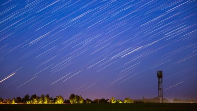 星星线在乡村景观上方的天空中移动。背景中的水塔。夜空上的星星轨迹。大曝光。天空中惊人的不寻常恒星效应