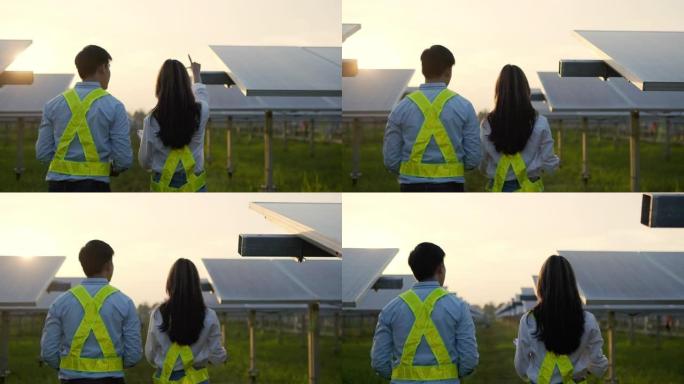 手持镜头，背光，后视图的亚洲年轻检查员工程师男人和女同事走在太阳能电池板的行之间，同时检查太阳能站的