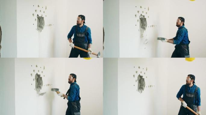 一个微笑的家伙用一根长棍子上的建筑锤拆除了房子里的一堵墙。装修过程中有趣的拆除公寓，摆脱不必要的墙壁