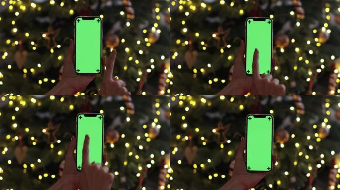 特写女人的手拿着色度键绿色屏幕触摸圣诞背景。使用带有绿色模型的电话，上网冲浪。