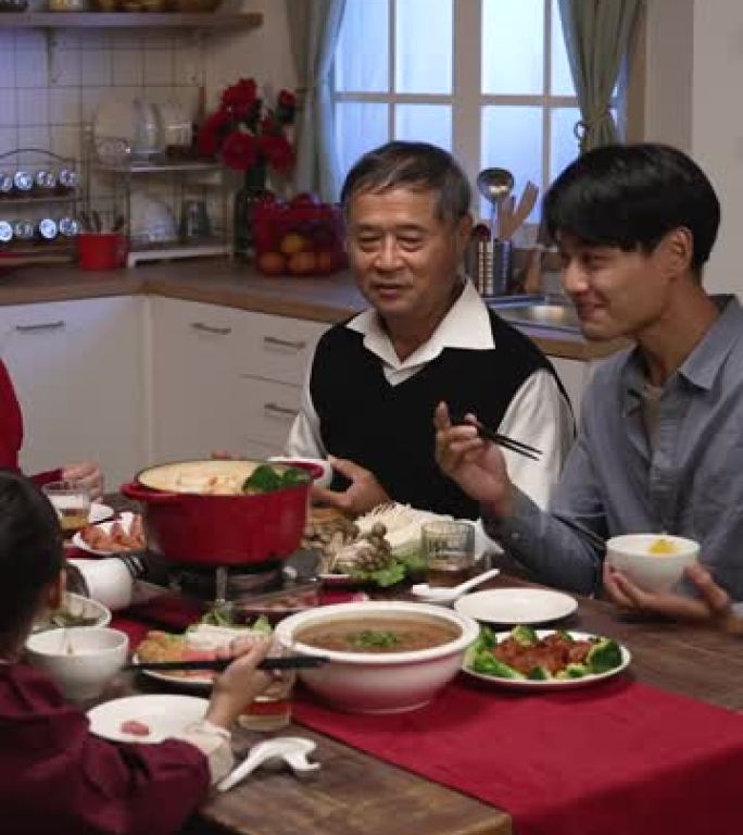 垂直屏幕: 快乐的亚洲大家庭在农历新年前夕在舒适的节日家庭室内吃团圆饭时嘲笑男人的笑话。中文文本翻译