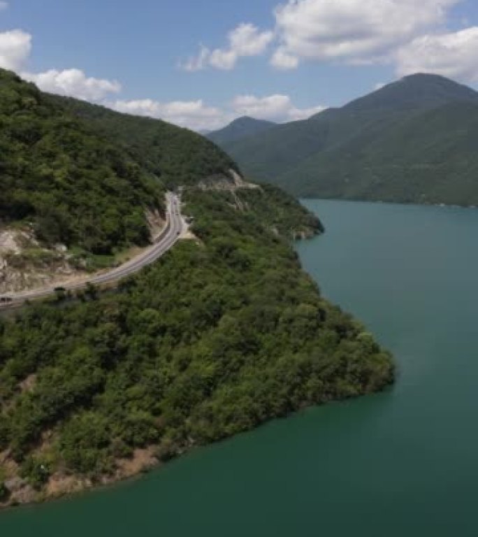 空中拍摄了一条海岸线道路，周围环绕着绿树，地平线上有山。