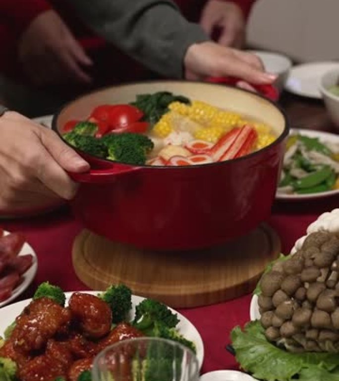 竖屏:亚洲媳妇和大妈在家里准备年夜饭时，在桌子上端着一锅热汤。文论阁翻译:财运