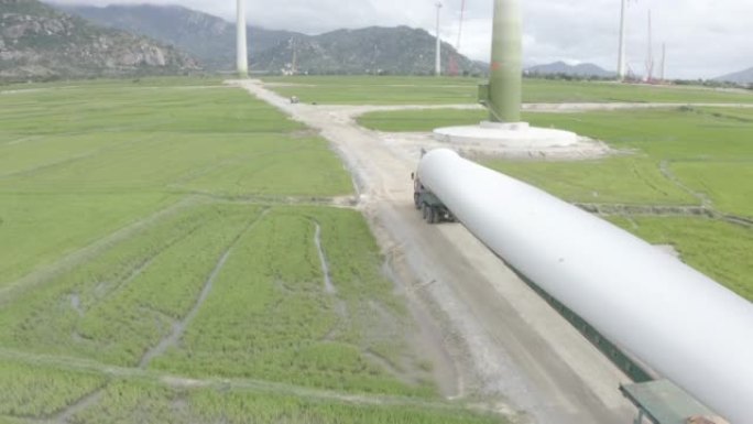 使用绿草场背景的长车辆进行风力涡轮机螺旋桨运输的航拍。风能发电塔的建造过程，以产生替代能源，