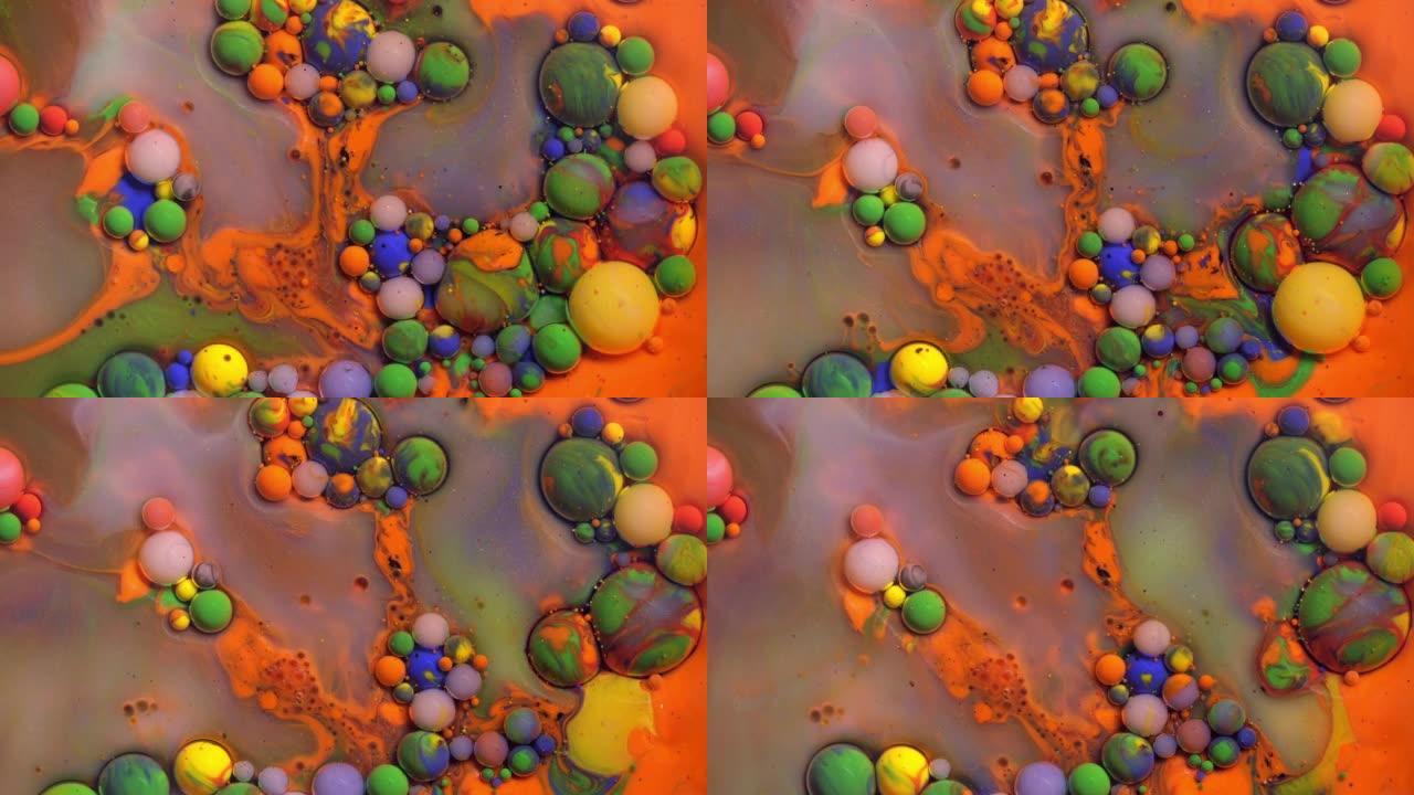 彩色丙烯酸涂料气泡在抽象设计中散布在橙色表面混合物上。金色闪闪发光的颗粒，墨球滴和混合。运动中的彩色