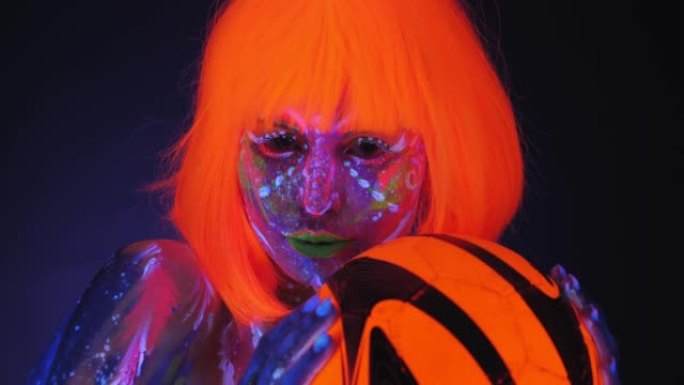 一名戴着亮橙色假发的紫外线人体艺术女子手持一个橙色球。