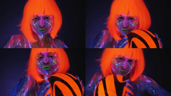 一名戴着亮橙色假发的紫外线人体艺术女子手持一个橙色球。