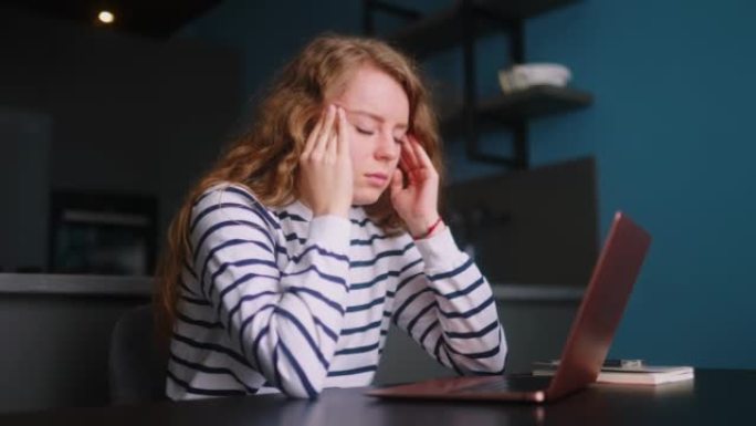 过度劳累的女人在家用笔记本电脑工作，按摩患有头痛的太阳穴。筋疲力尽的女士在使用电脑远程工作后感到眼睛