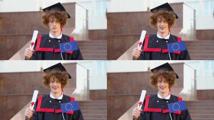 一位硕士生的卷发有趣的微笑毕业生拥有完成学业的文凭和欧盟的旗帜，并打哈欠