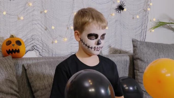男孩被装饰为骷髅在家里玩庆祝万圣节的气球。