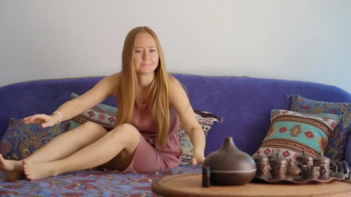 一位年轻女子正坐在平板电脑的沙发上。她开始被蚊子咬了。她用特殊的防蚊油混合物将香气扩散器变成。现在她