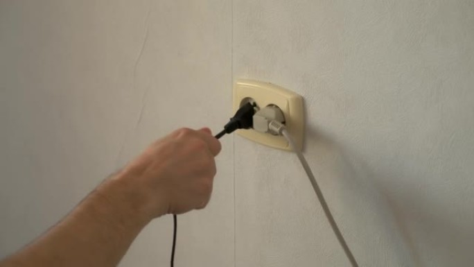 人的手将电器的插头叉关闭到插座中。