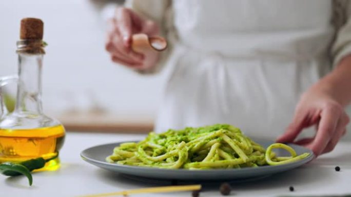 女孩厨师在盘子上的绿色意大利面上撒盐，意大利面用绿色酱汁煮熟