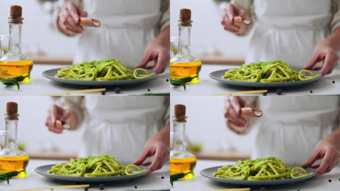 女孩厨师在盘子上的绿色意大利面上撒盐，意大利面用绿色酱汁煮熟