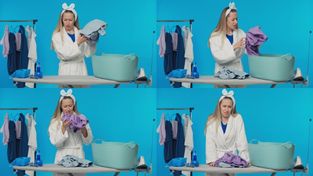 一个女孩站在工作室的蓝色背景下。女人嗅着躺在洗衣碗里的衣服