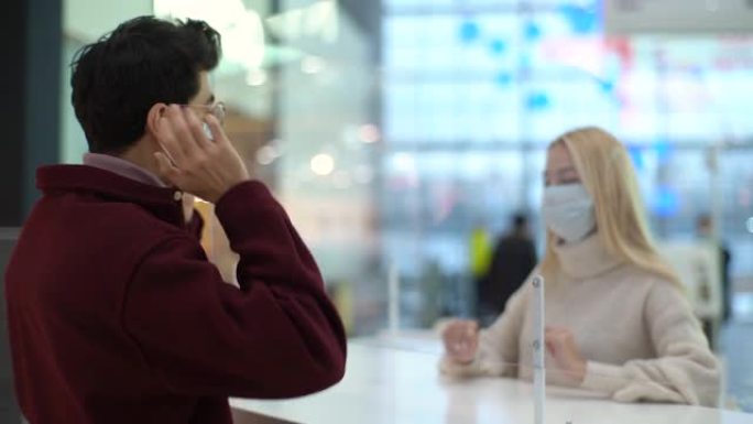 漂亮的女性员工戴着防护口罩给男性客户戴口罩，站在商场大厅的玻璃隔断交谈。