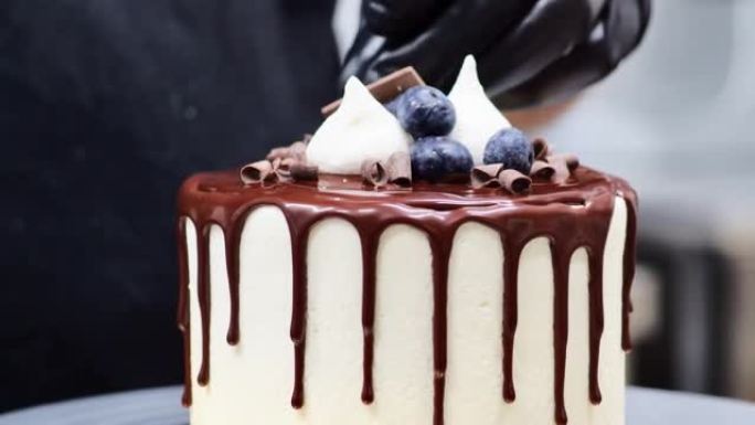 蛋糕设计师用浆果蛋白酥皮巧克力装饰磨砂滴蛋糕顶部