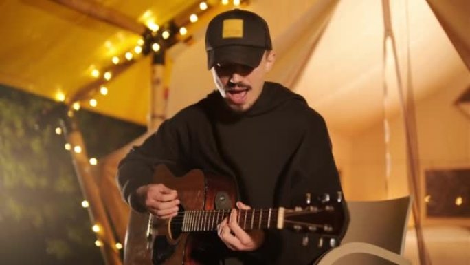 男子在带灯泡的帐篷里弹吉他唱歌