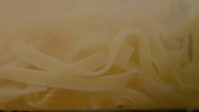 在慢动作的透明锅中，将意大利细面条与叉子混合在一起。