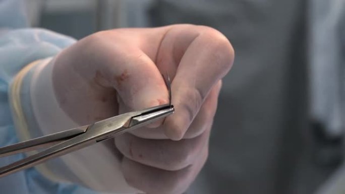 外科医生用一只手在沾满鲜血的医疗手套中穿针引线。医生正准备缝合手术切口。行动结束的概念。