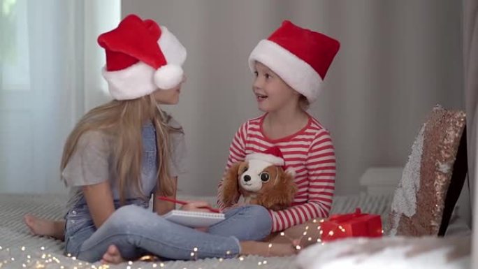 戴着红色圣诞帽的两个姐妹女孩给圣诞老人写了一封信