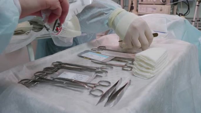 宠物手术的开始。外科医生从桌子上拿了一把手术刀。助手打开无菌湿巾的包装，并用仪器将其放在桌子上。