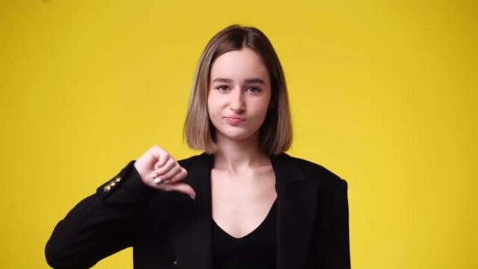可爱的女孩在黄色背景上展示拇指向下的4k视频。